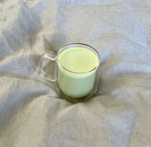 Load image into Gallery viewer, Double walled glass mug that can hold 350ml. Contains a matcha latte, sitting on a sage green duvet.

